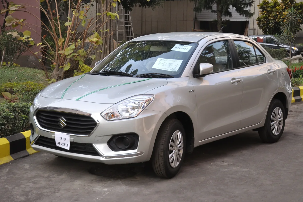 A silver Maruti Suzuki Dzire saloon parked beside a building
