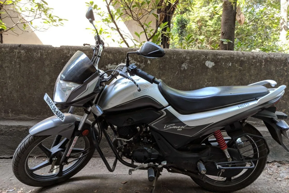 A silver and black Hero Splendor motorcycle parked against a wall