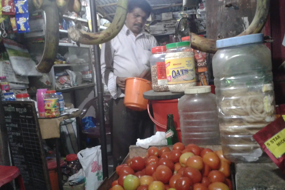 A shopkeeper at work in a small grocery store with jars, packets and tomatoes in front