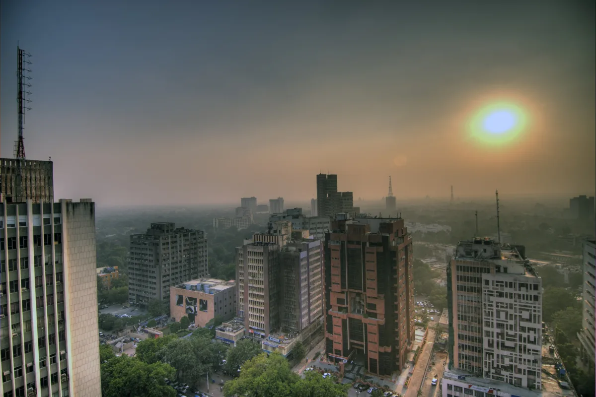 A hazy orange sun over office towers in central Delhi, with smog over the skyline