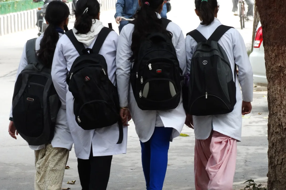 Four women medical students in white coats with backpacks walking along a campus path