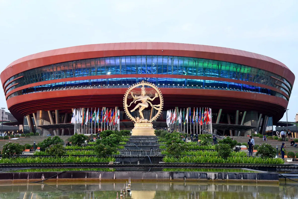 The curved Bharat Mandapam convention centre in New Delhi with a large Nataraja statue and flags in front