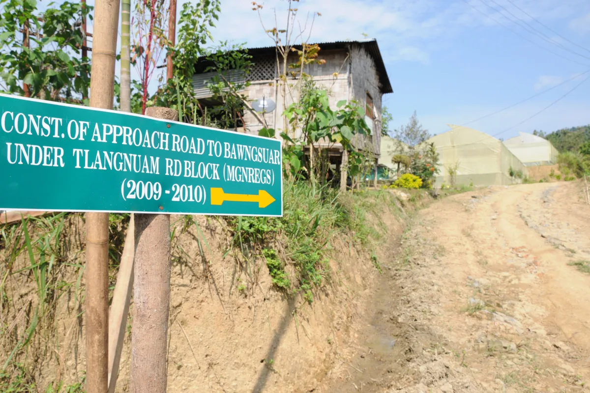 A signboard for a rural approach road built under MGNREGS beside a dirt road in Mizoram