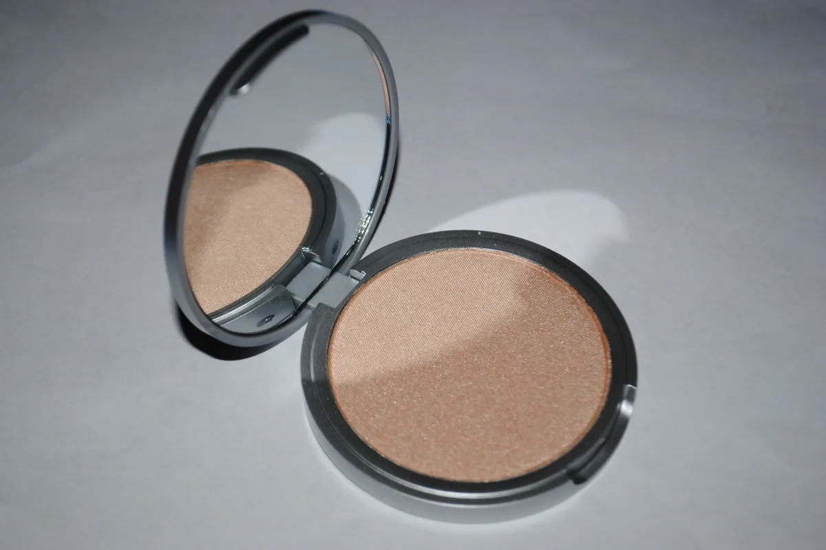 An open make-up compact with a shimmering powder and a round mirror