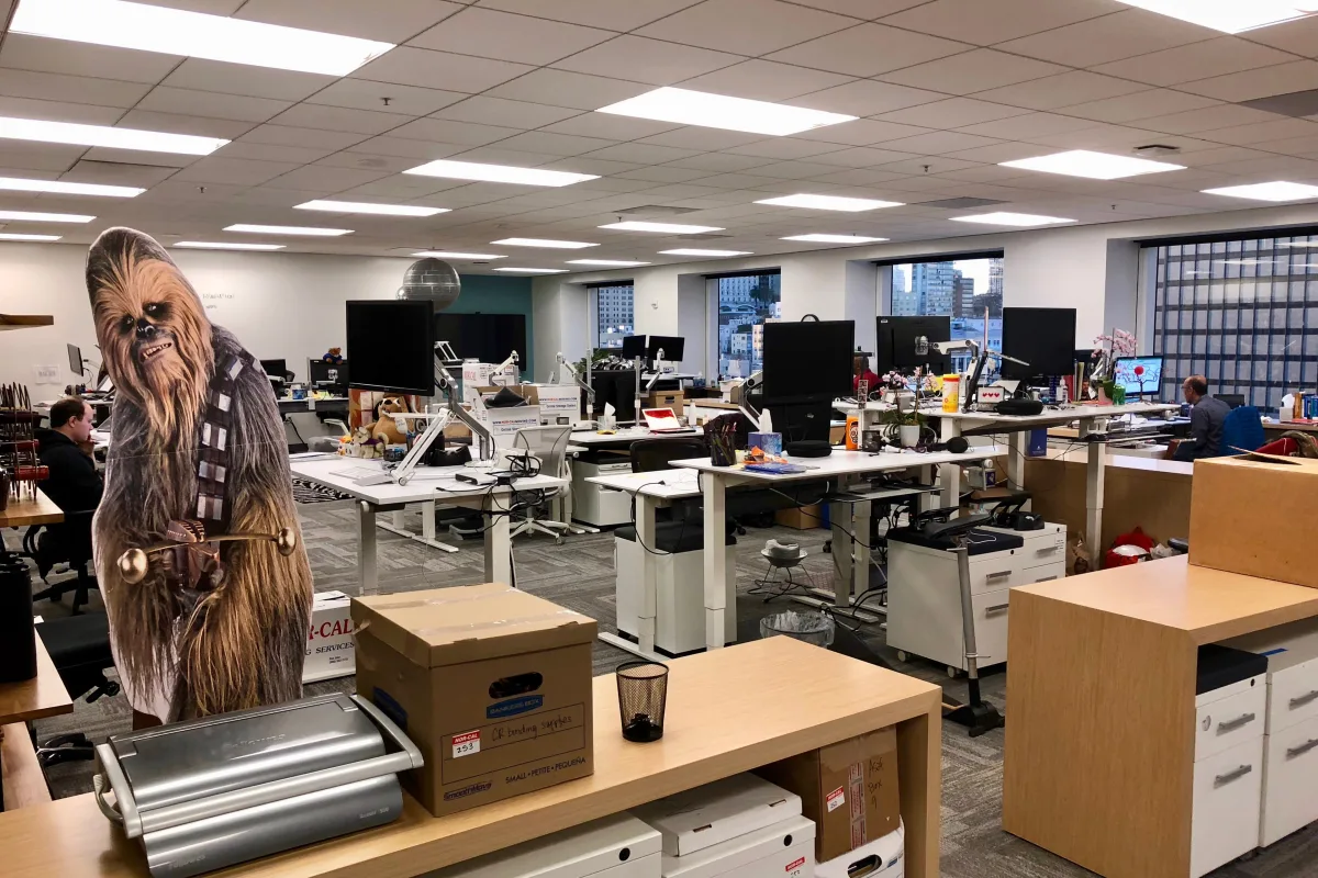 Rows of desks and monitors in an open-plan office, with a life-size Chewbacca figure in the foreground