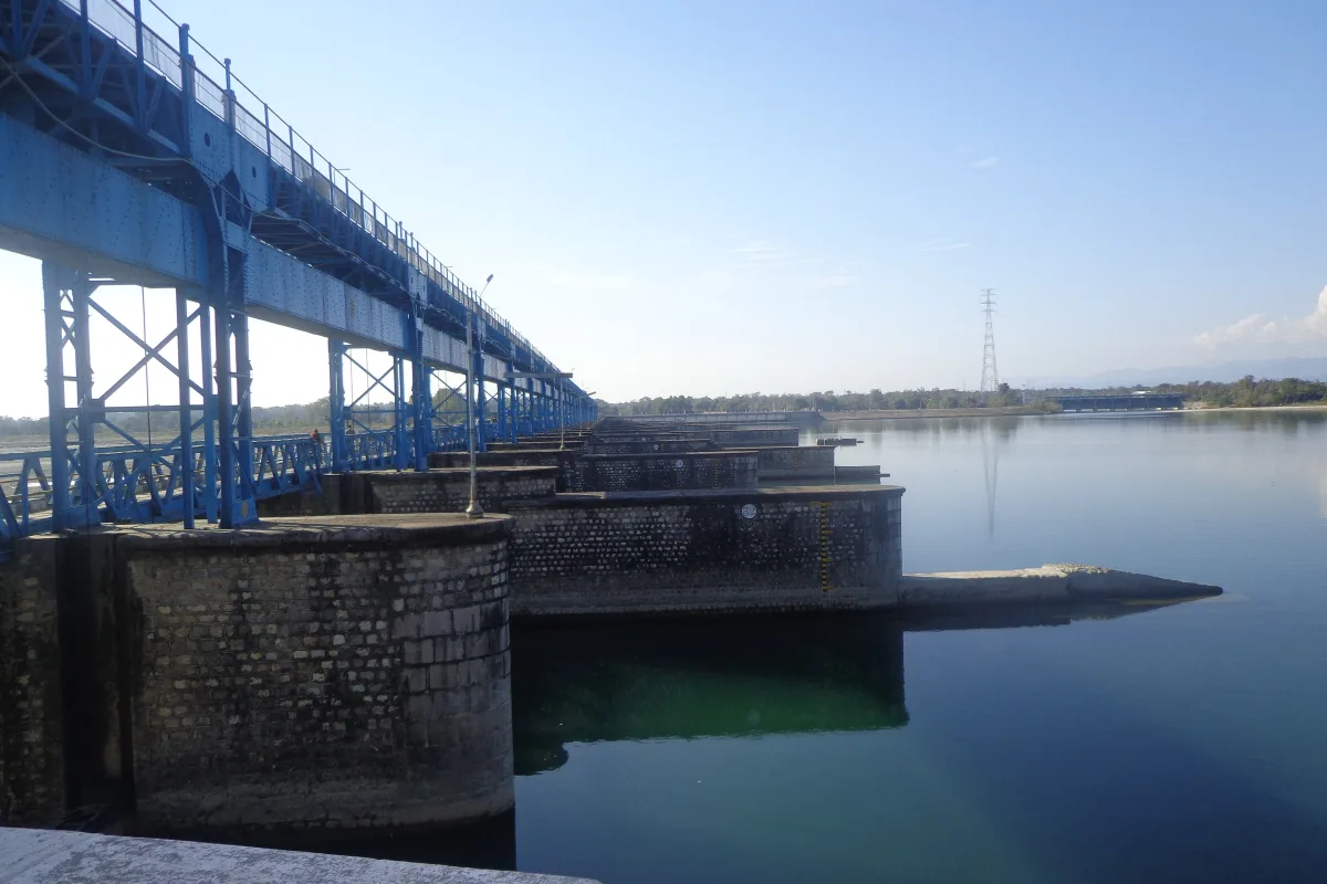 A long steel bridge over the barrage and wide still water at Banbasa under a blue sky